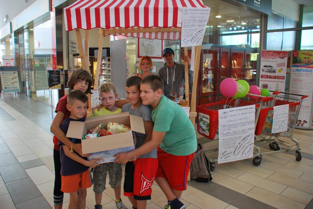 Otroci pozirajo s škatlo doniranih živilskih izdelkov na humanitarni akciji zbiranja hrane.